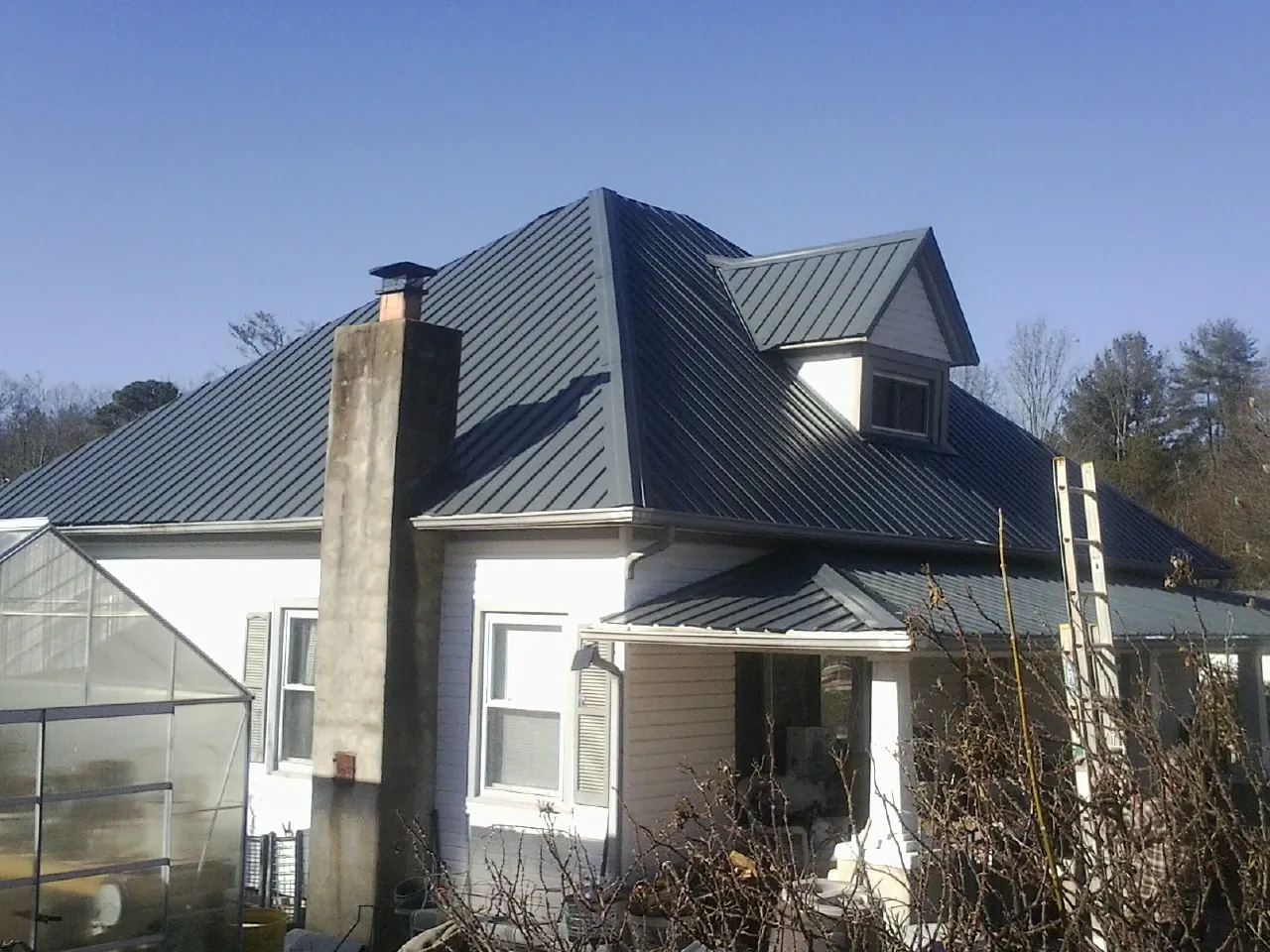 Dark blue standing seam metal roof on a white farmhouse with dormer — Slate & Tile Roof Repair by Roofing Brothers in Midway City