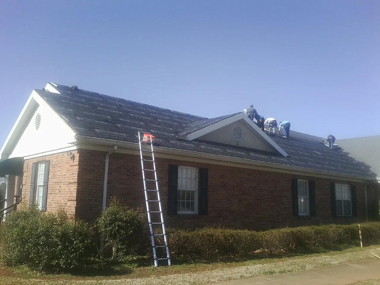 Crew tearing shingles off a brick ranch roof with a ladder set — Emergency Roof Repair work by our crew in Midway City