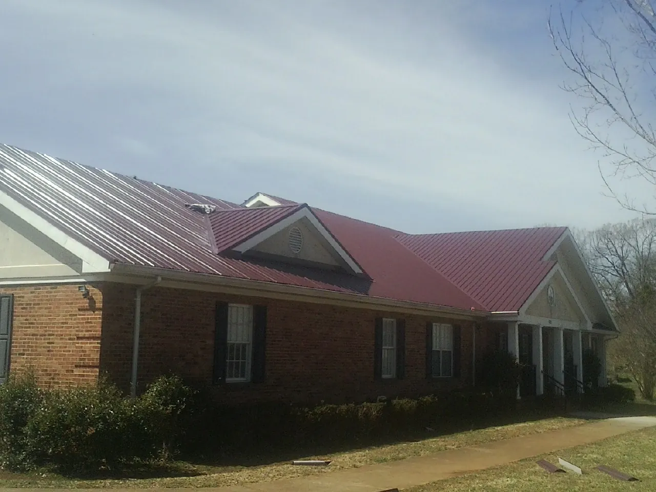 Red metal roof with gabled entries on a long brick building, from a Hail Damage Roof Repair job in Midway City