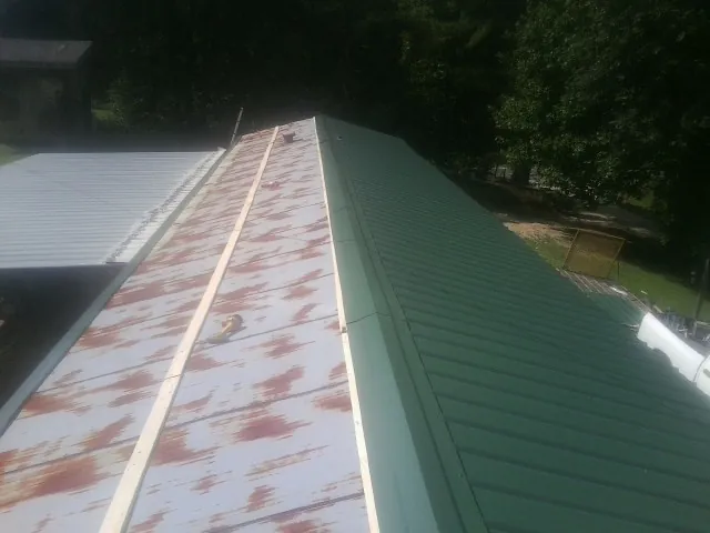 Old rusted panels beside newly installed green metal roofing — Wind Damage Roof Repair by Roofing Brothers in Midway City