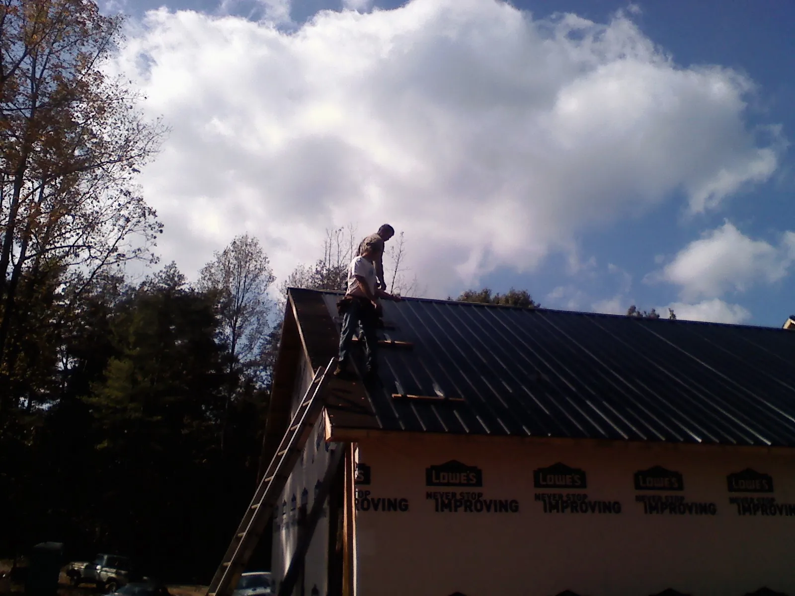 Roofer fastening dark metal panels high against a cloudy sky, from a Roof Inspection job in Midway City