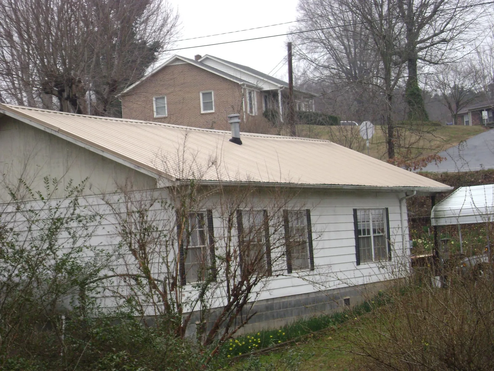 Tan metal roof on a white sided house set into a hillside — Commercial Roofing by Roofing Brothers in Midway City