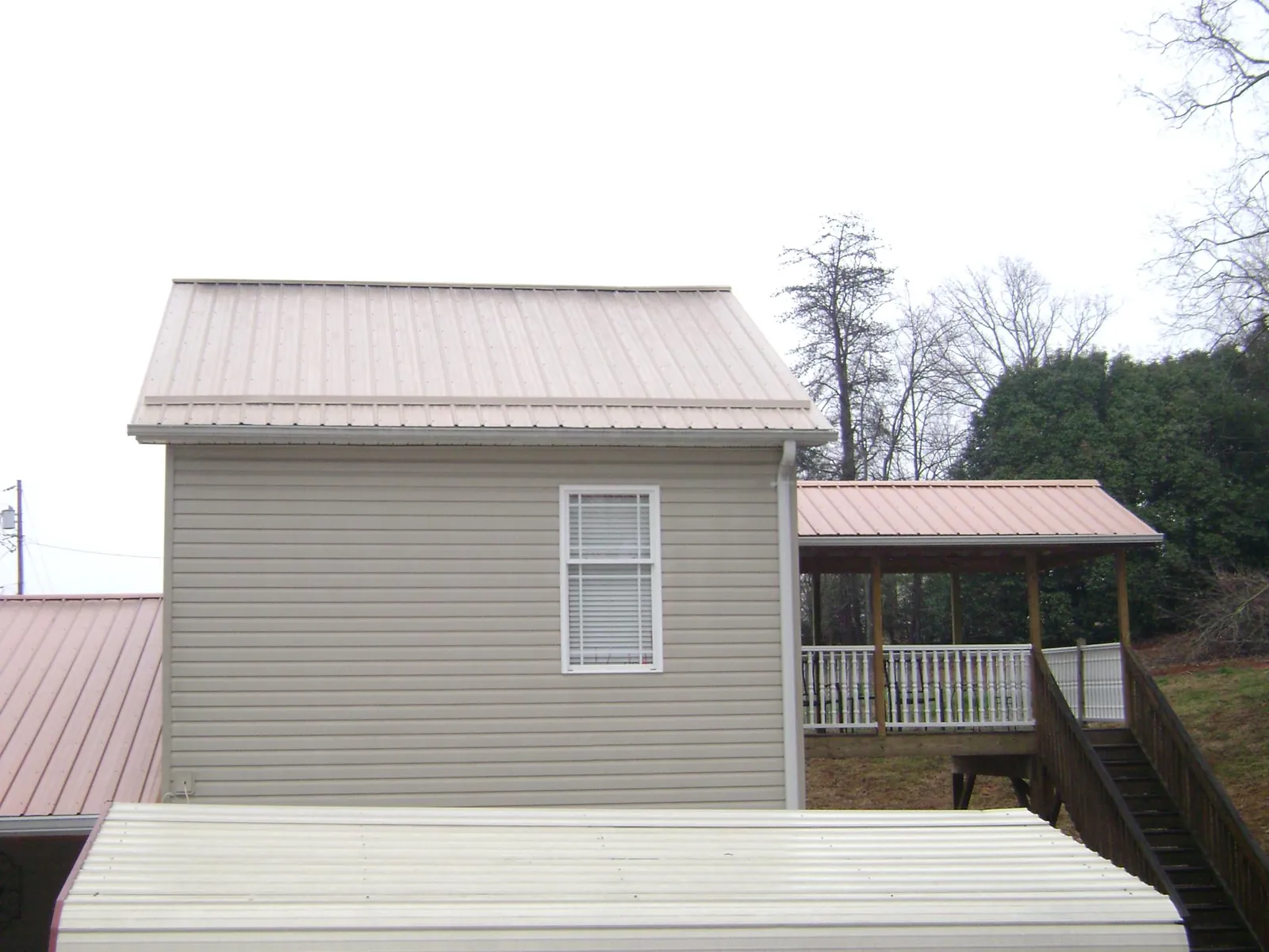 Tan metal roofs on a two story addition and attached porch, from a Roof Replacement job in Midway City
